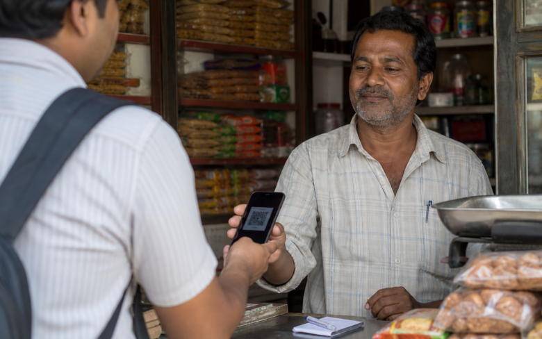Comerciante mostrando un código QR de cobro mientras un cliente confirma una transferencia en su teléfono.